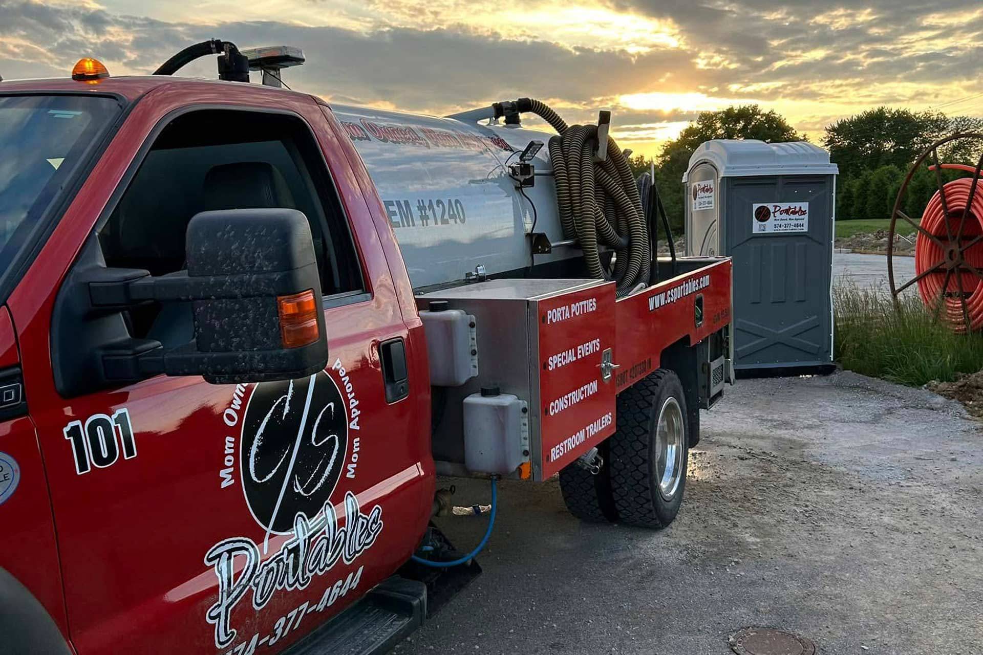 Red sanitation truck servicing a portable toilet at sunset.